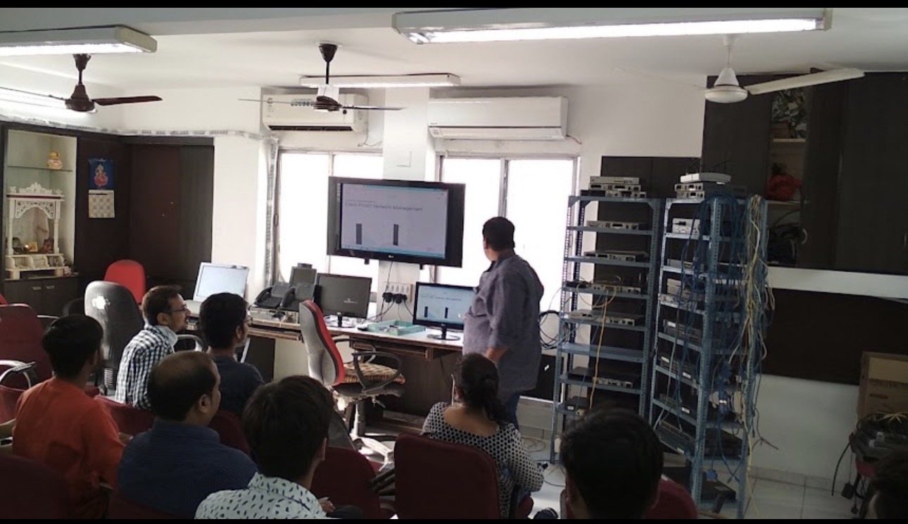 A Cisco networking class in progress beside the physical lab racks at Attila Technologies, Ahmedabad