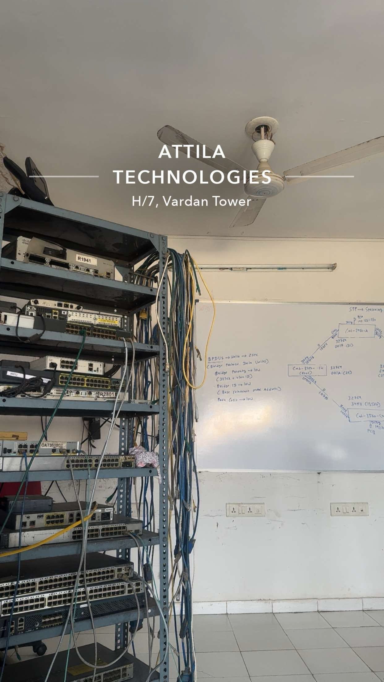 Cisco routers and switches on the lab rack, beside a whiteboard of spanning-tree (STP) notes